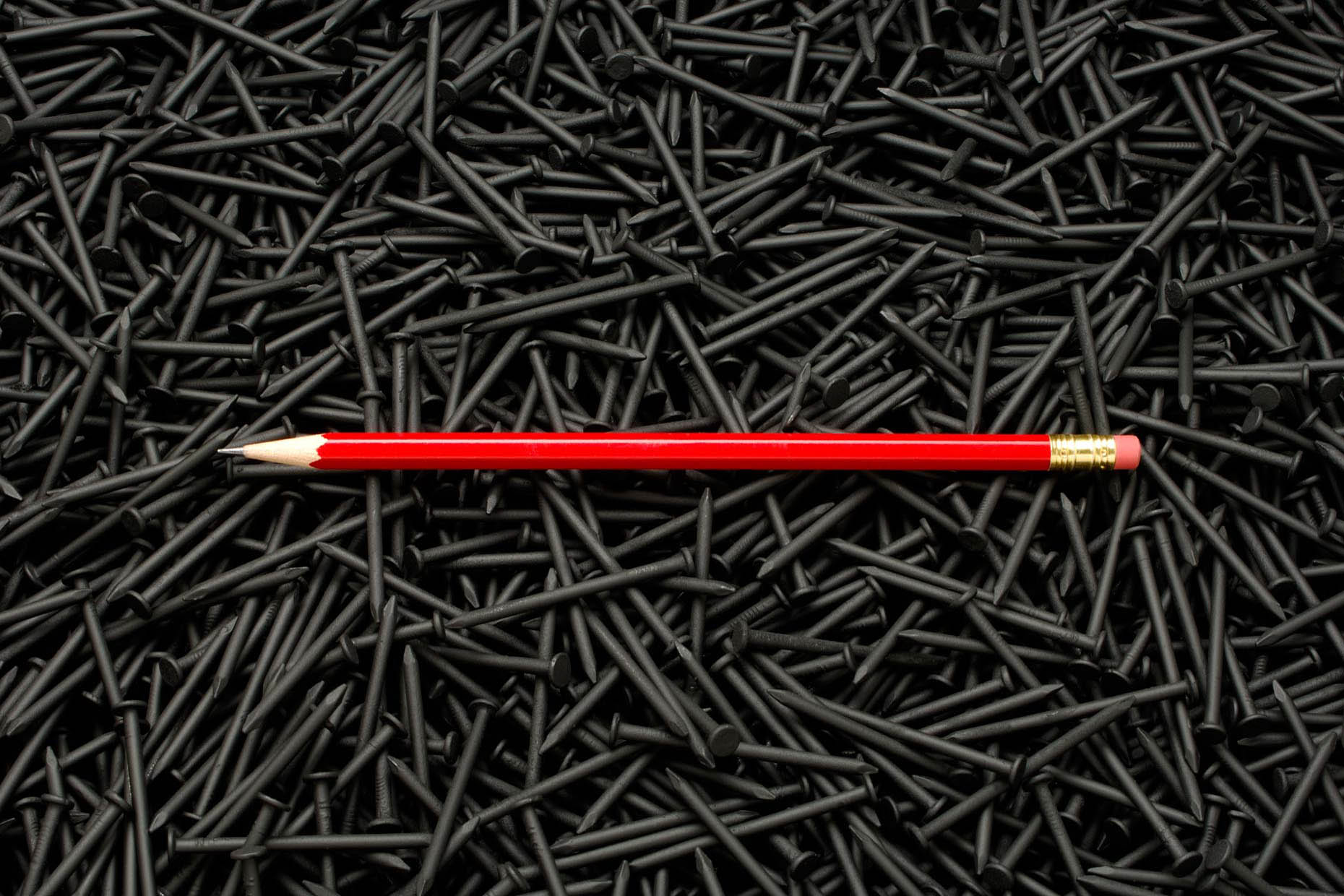 A sharp red wooden pencil and a background of black metal nails. Dangerous writing nailed it